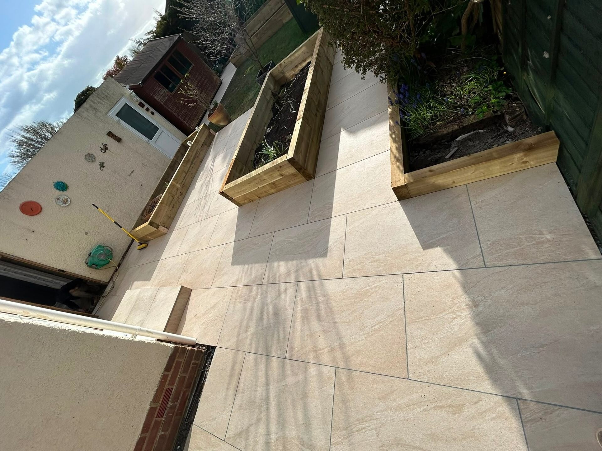 Cream porcelain patio with sleek raised planters and slabbed steps in a Littlehampton back garden.