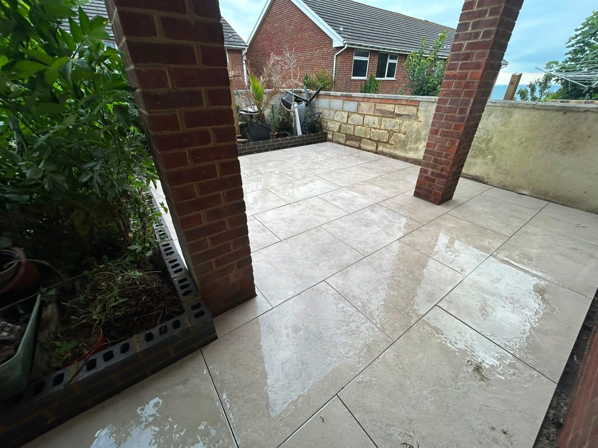 Cream porcelain patio installed around retained brick pillars at a Sussex home.