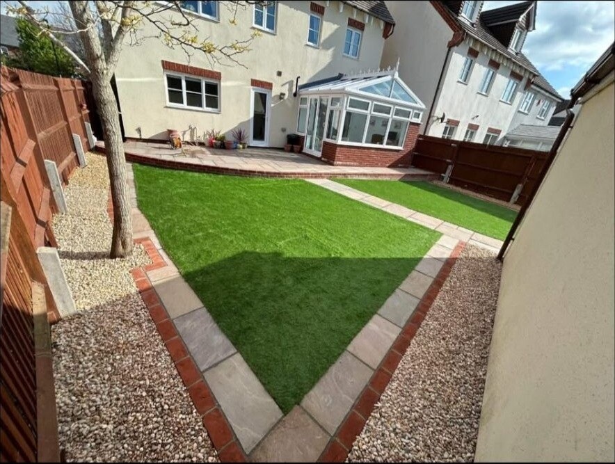 Red clay-brick path with planted borders running through a side garden.