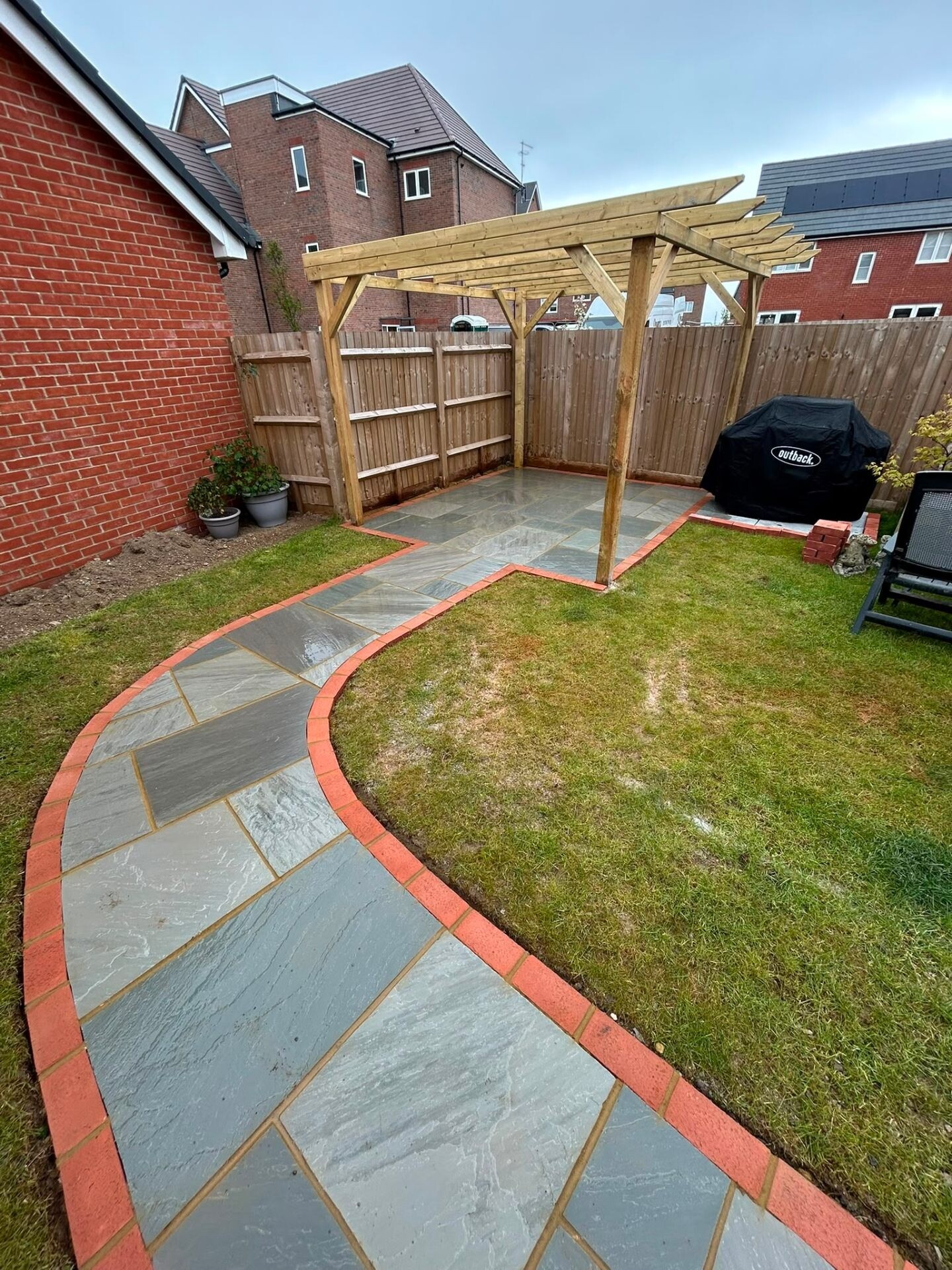 Curved sandstone path with brick edging and lawn in a redesigned garden.
