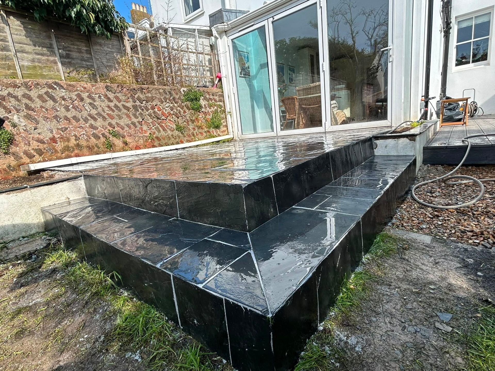Polished black slate patio with crisp jointing and a reflective wet finish.