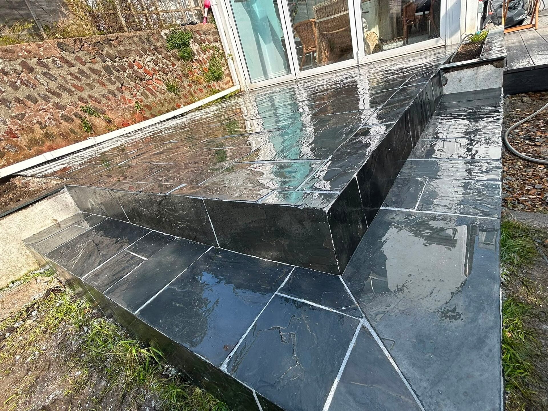 Polished black slate patio with mitred step risers and a wet-look finish.