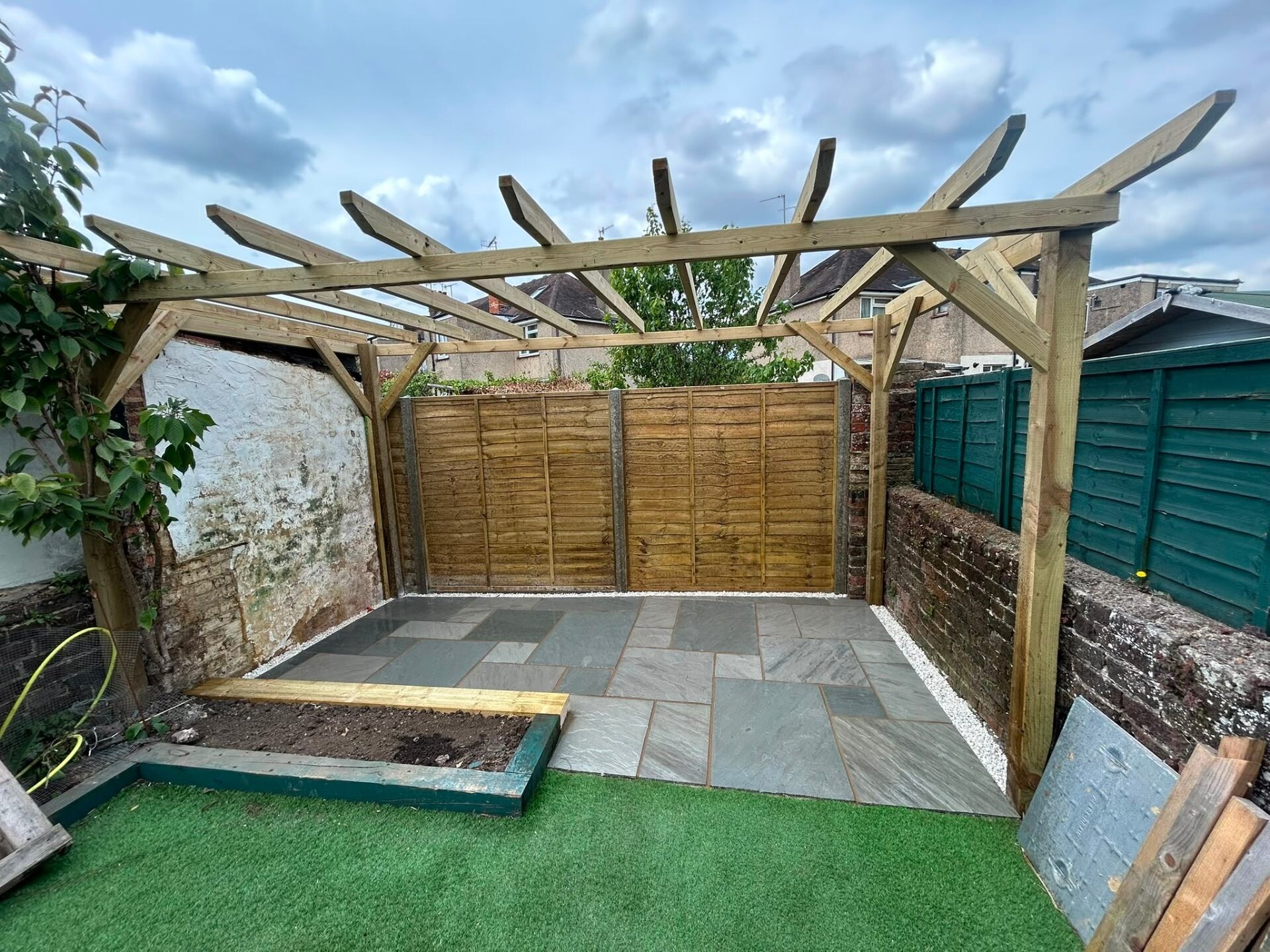 Porcelain patio with a timber pergola and artificial grass strip in a low-maintenance garden.